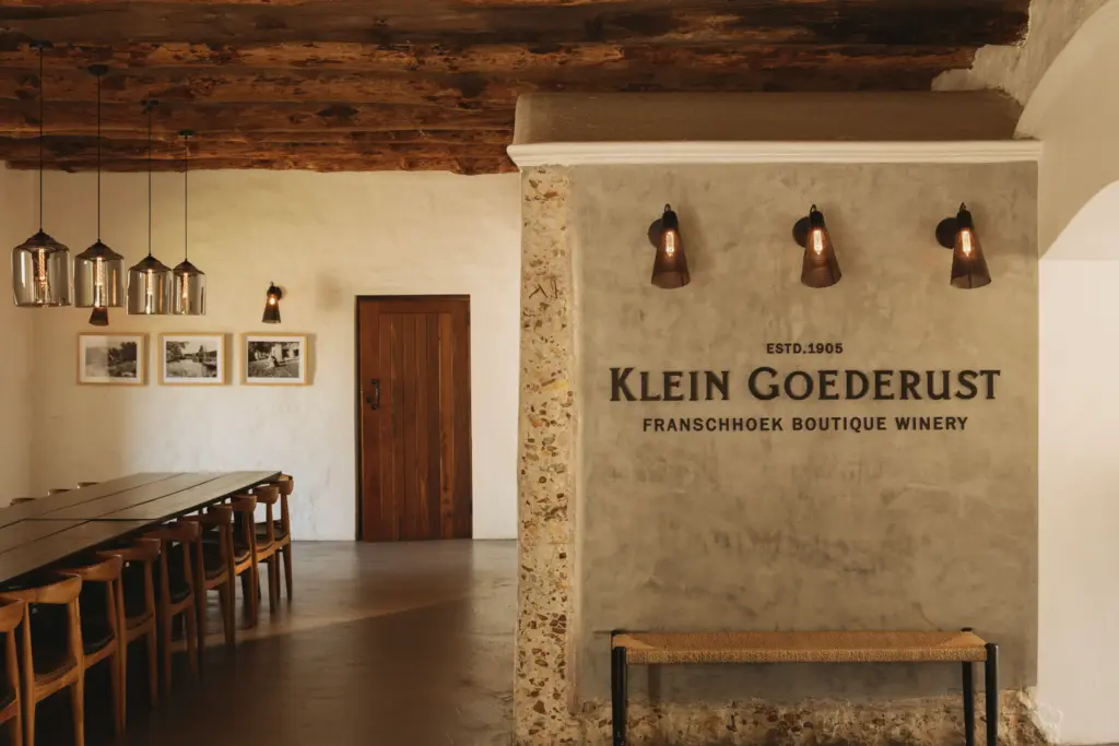 The Klein Goederust Franschhoek tasting room with a long communal table and estate name on the wall